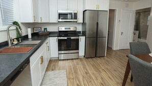 A modern kitchen with white cabinets, stainless steel appliances, a black countertop, and a wooden floor.