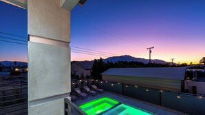 A swimming pool with a green light, surrounded by lounge chairs and a view of mountains at sunset. - Spacious New Build - Heated Pool, Covered Patio, Sunsets, Games, Luxurious Space (Desert Hot Springs)