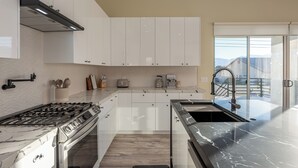 A modern kitchen with white cabinets, a gas stove, and a marble countertop. - Spacious New Build - Heated Pool, Covered Patio, Sunsets, Games, Luxurious Space (Desert Hot Springs)