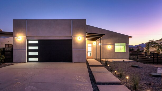 A modern house with a garage, a covered driveway, and a landscaped garden with small plants and lights. - Spacious New Build - Heated Pool, Covered Patio, Sunsets, Games, Luxurious Space (Desert Hot Springs)