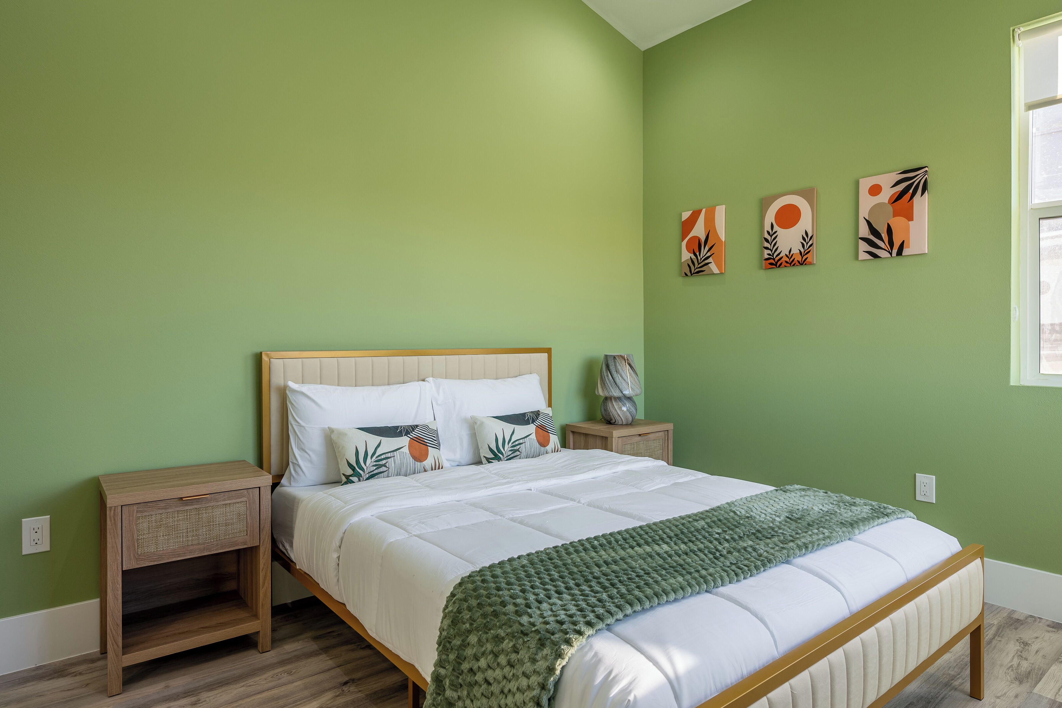 A bedroom with a bed, nightstands, and artwork on the wall.