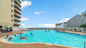 A swimming pool with people swimming and lounging, surrounded by a brick deck and a building with balconies. - Snowbirds Land on the 29th Floor for the Winter (Panama City Beach)