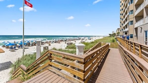 A wooden boardwalk leading to a beach with umbrellas and lounge chairs. - Snowbirds Land on the 29th Floor for the Winter (Panama City Beach)