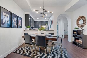 A modern dining area with a long table, black chairs, and a chandelier.