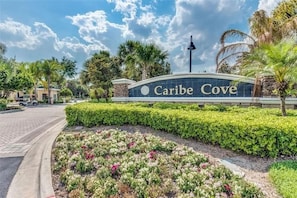 A landscaped area with a sign reading "Caribe Cove" and a curved pathway leading to a building.