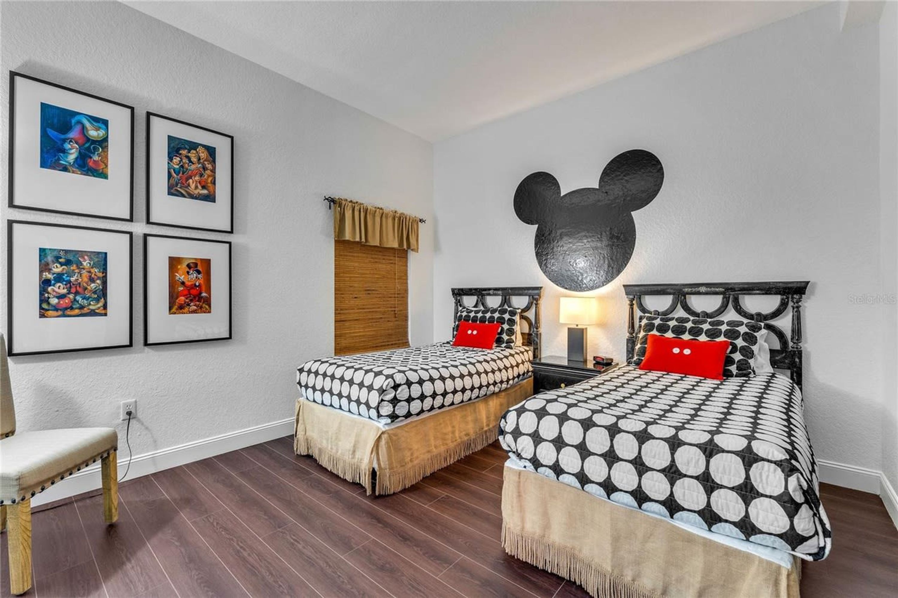 Un dormitorio con dos camas, un adorno con la figura de Mickey Mouse, cuadros enmarcados en la pared y suelo de madera.