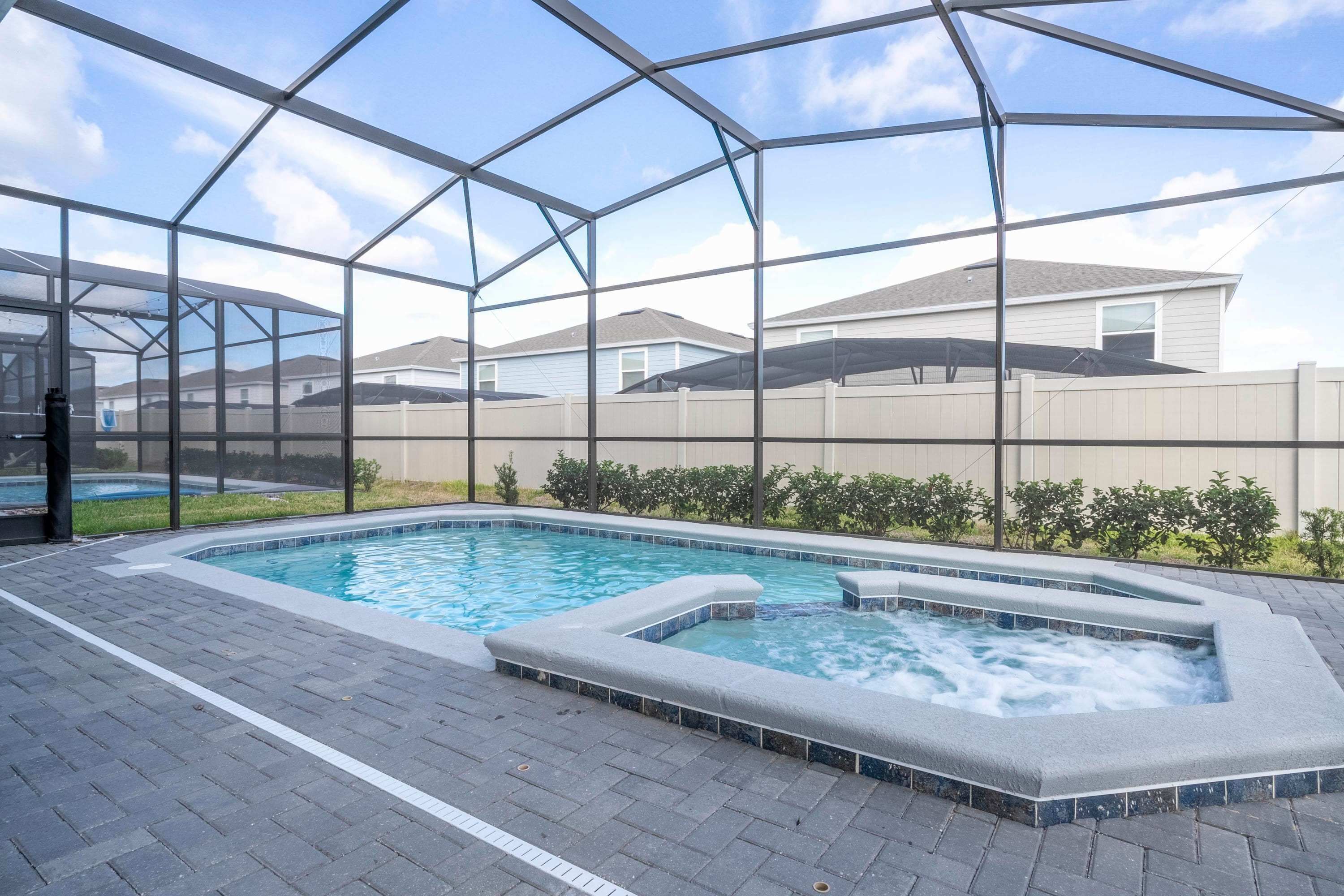 A swimming pool with a hot tub, surrounded by a glass enclosure, with a view of houses in the background.