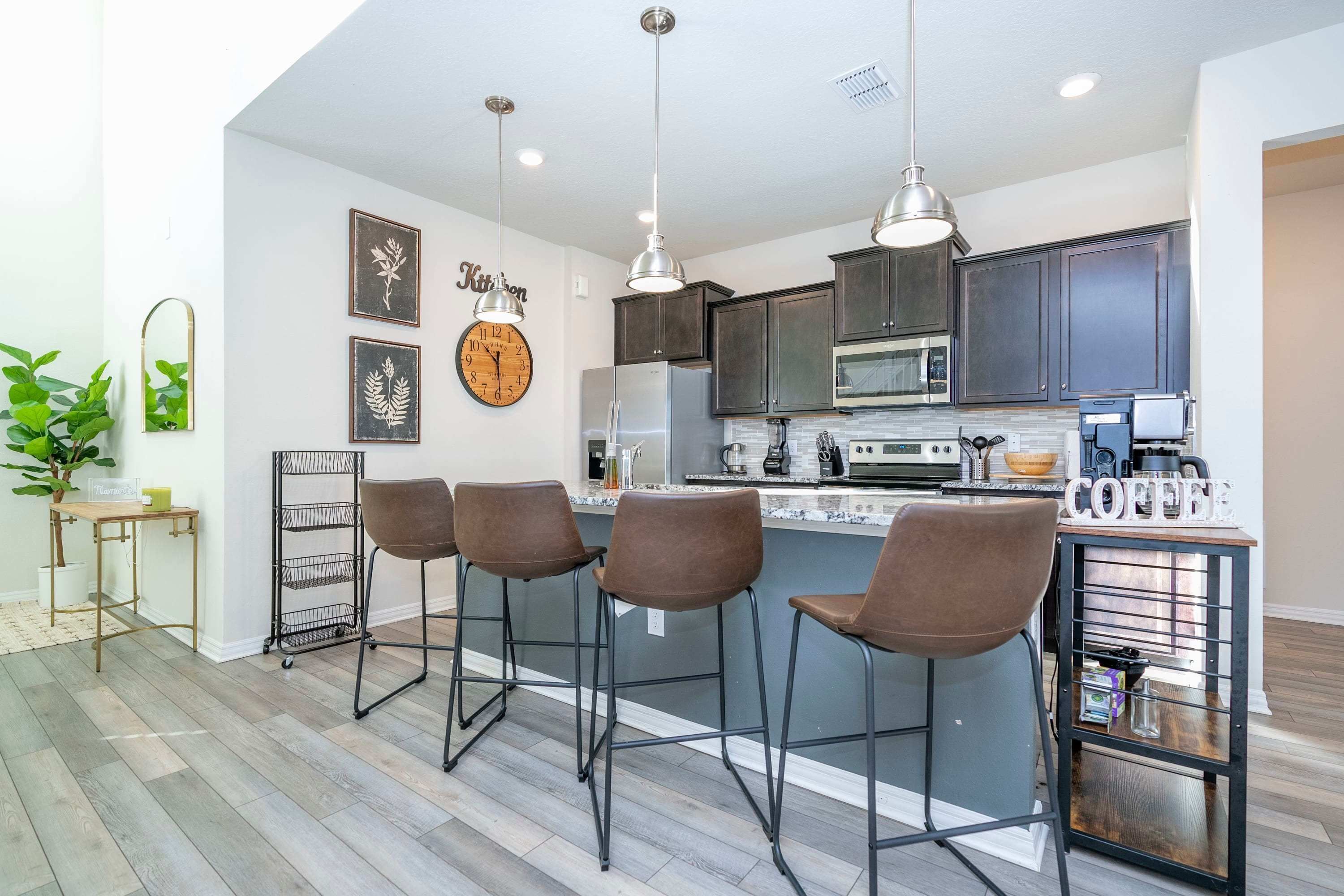 A modern kitchen with a central island, bar stools, pendant lighting, and a clock on the wall.