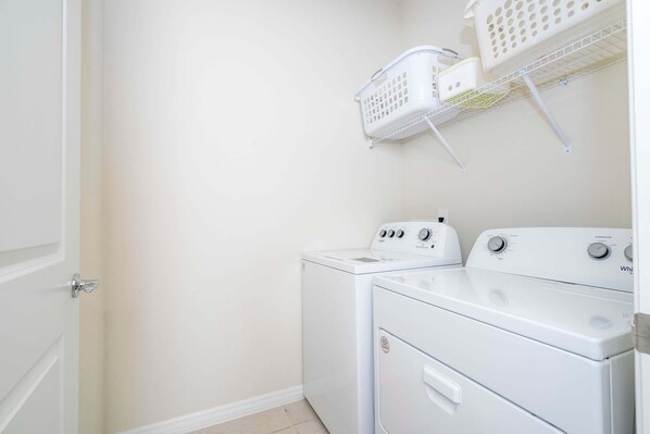 A laundry room with two white washers and dryers, a white door, and a wall-mounted laundry basket.