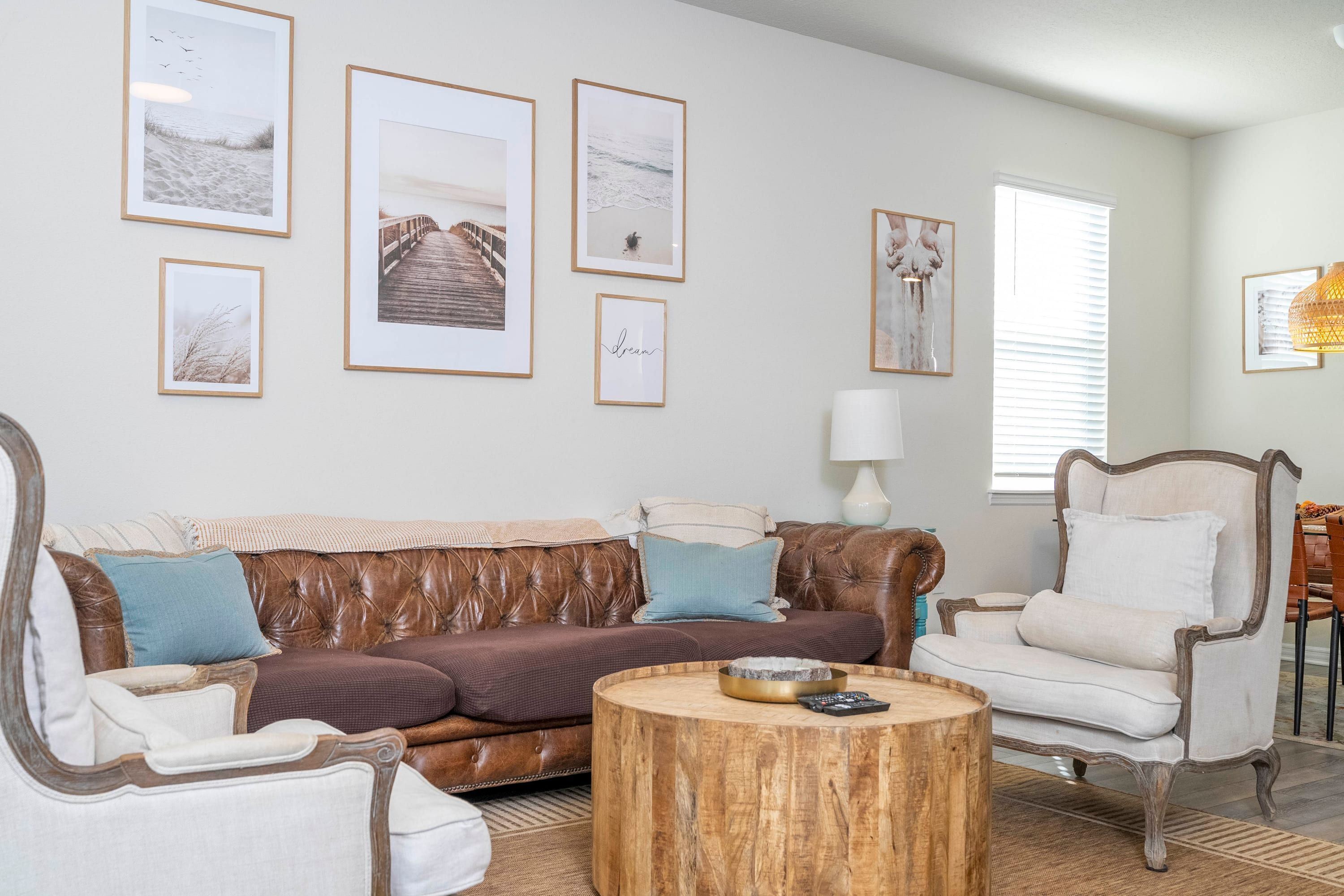 A living room with a brown leather sofa, a white armchair, a round wooden coffee table, and framed pictures on the wall.