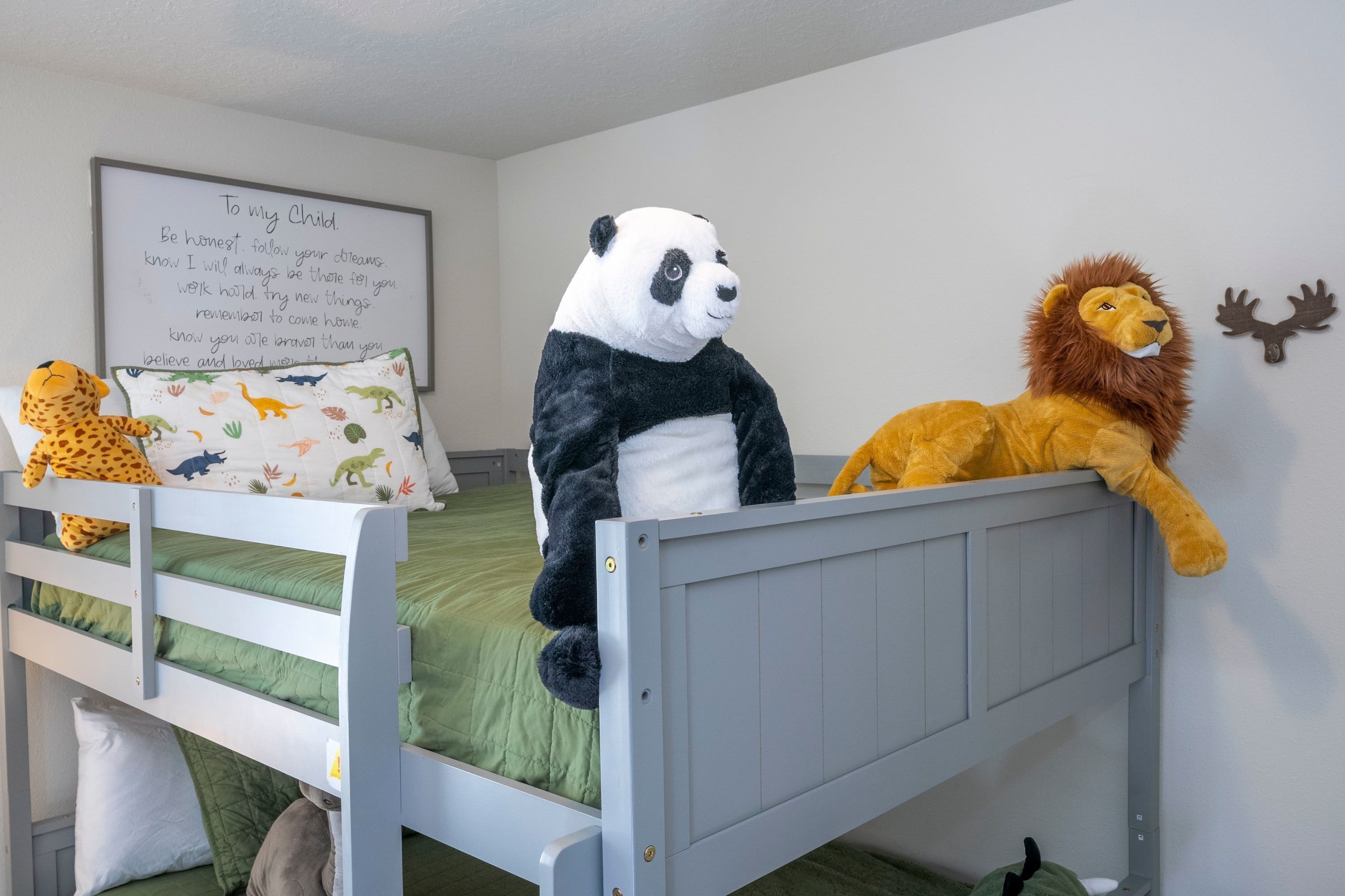Une chambre d’enfant avec un lit superposé, des peluches, une affiche motivante et une décoration en forme de bois de cerf.