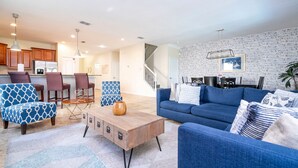 A modern living room with a blue sofa, patterned armchairs, and a wooden coffee table. A kitchen with wooden cabinets and a refrigerator is visible in the background. - Free Pool Heat if you Stay in the Month of November (Davenport)