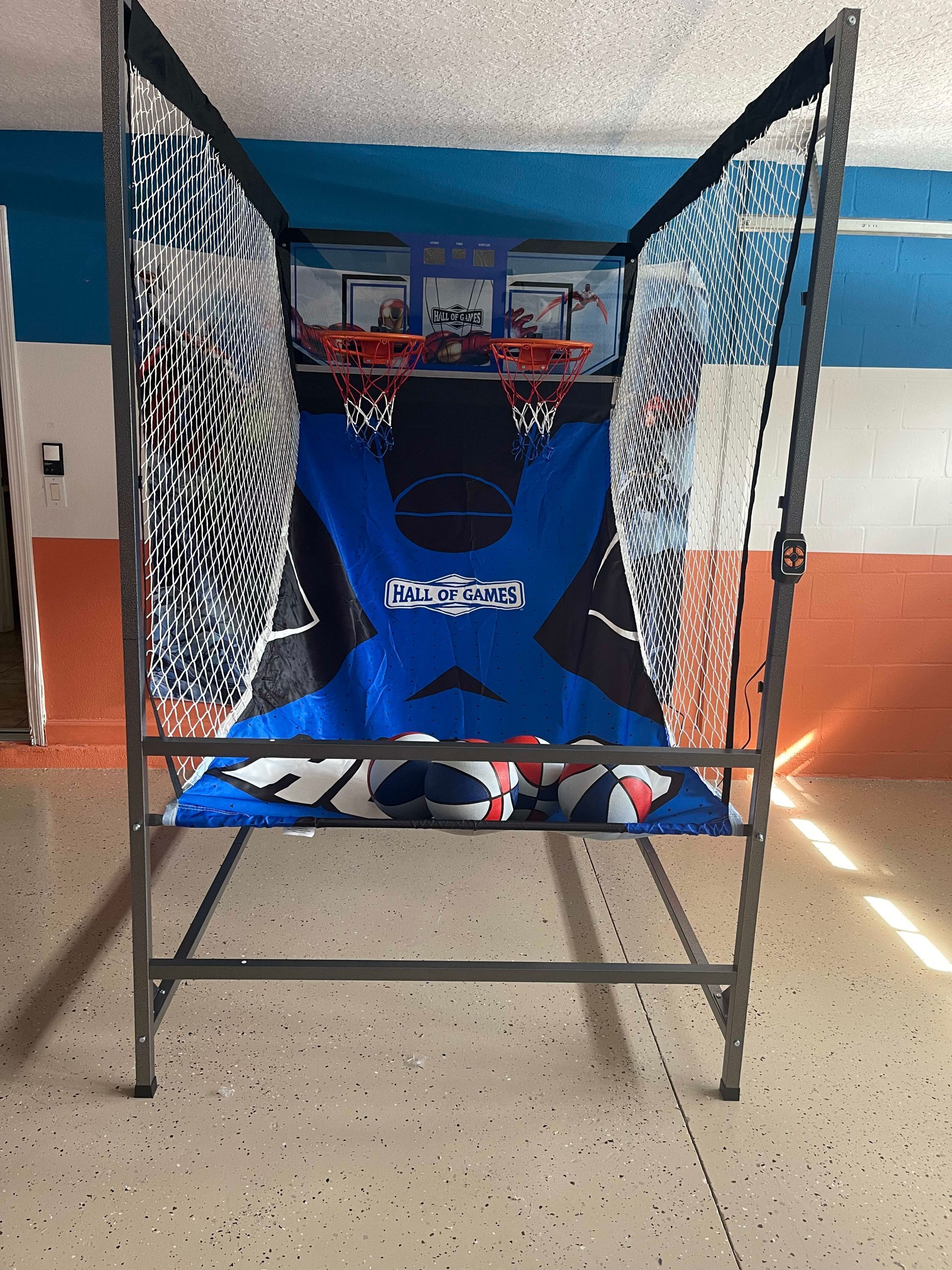 En basketkorg med nät, placerad framför en vägg med blå och orange ränder.