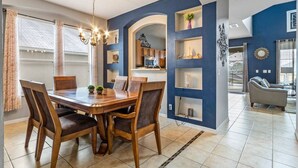 Un comedor con una mesa y sillas de madera, una araña y vista a la cocina.
