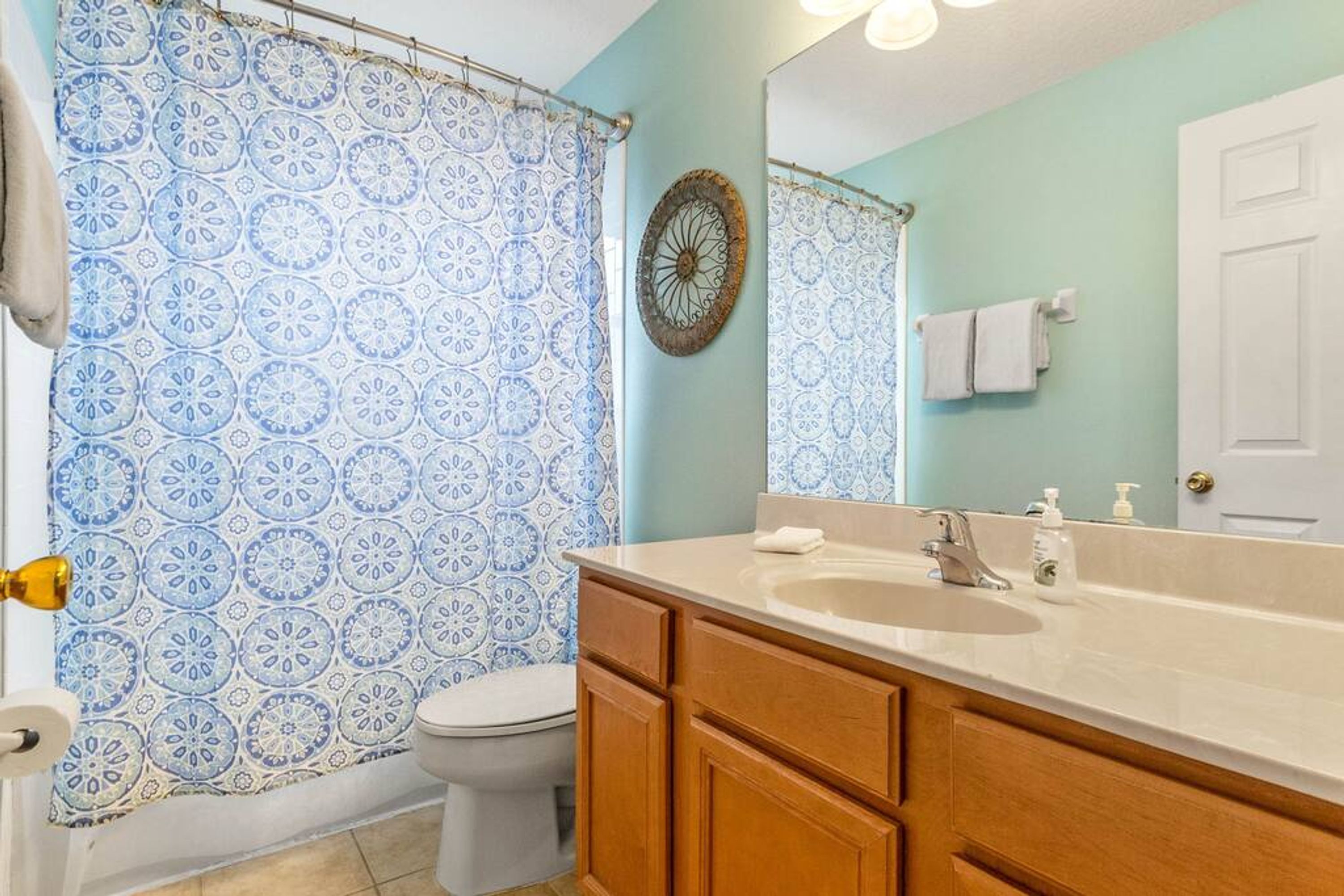 A bathroom with a patterned shower curtain, a sink with a mirror, wooden cabinets, and a toilet.