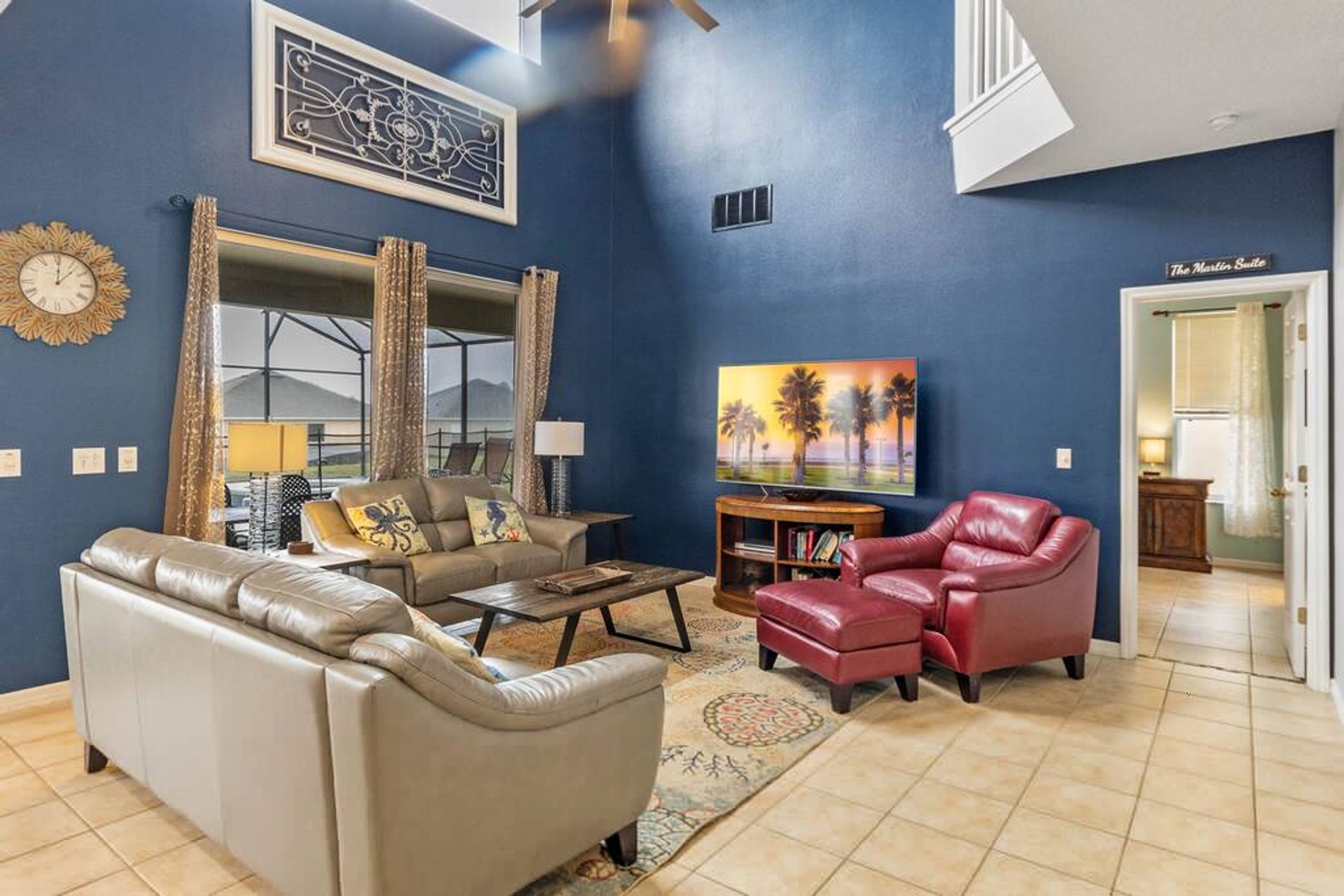 A living room with a sofa, armchair, coffee table, and a TV. There is a painting on the wall and a window with curtains.