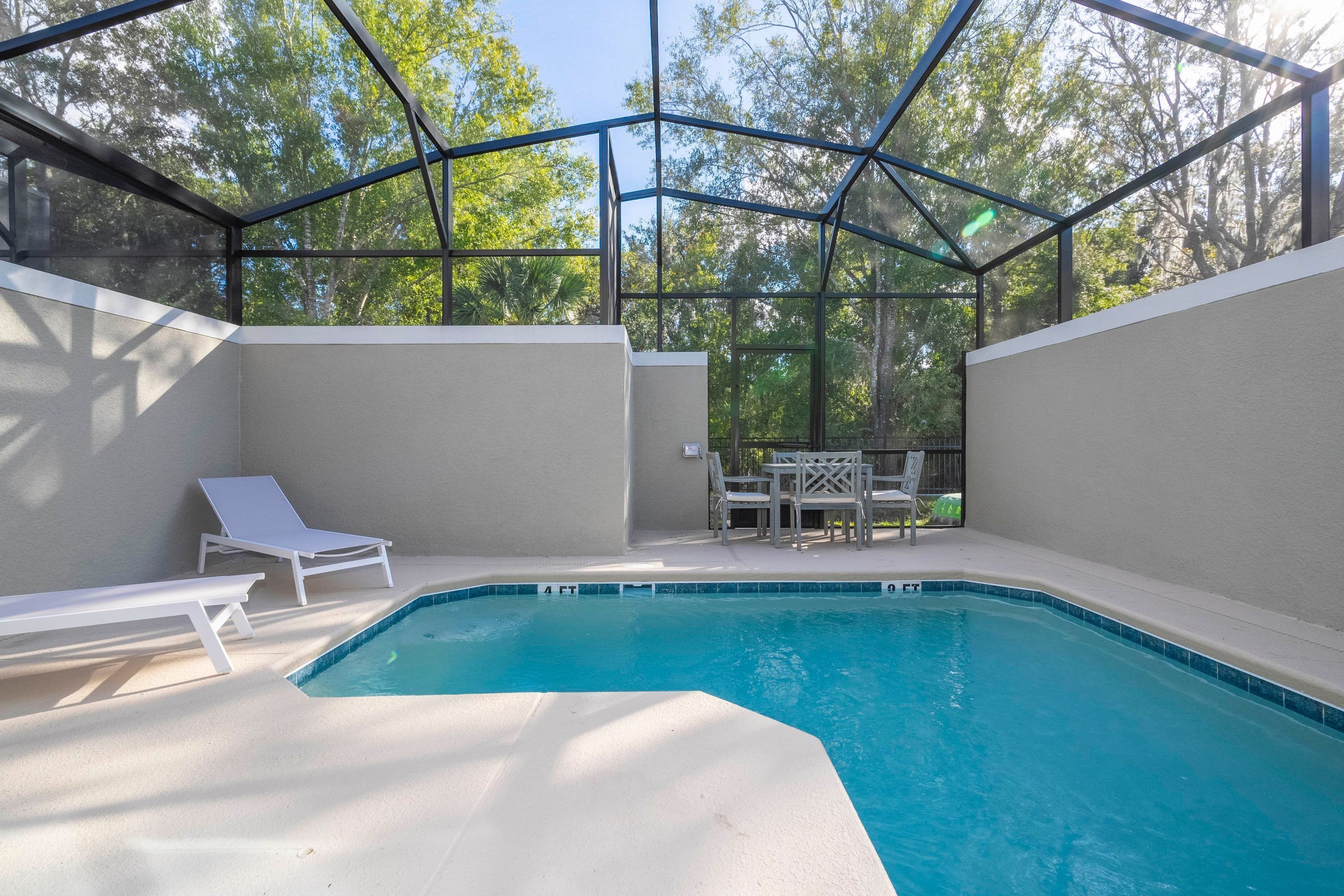 Ein Swimmingpool mit Glasveranda, umgeben von weißen Liegestühlen und einem Tisch.