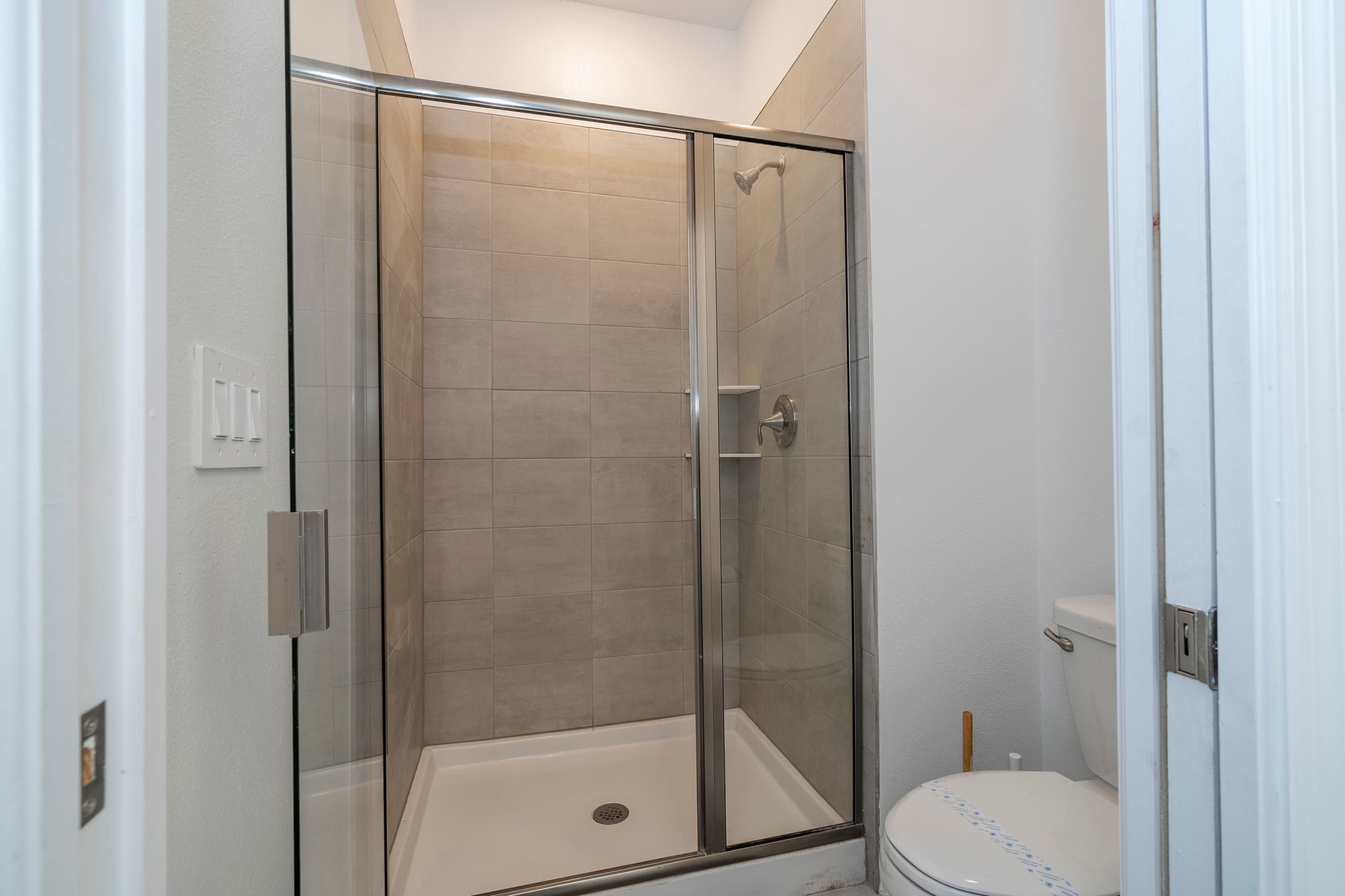 A glass-enclosed shower stall with a white toilet and a visible light switch on the wall.