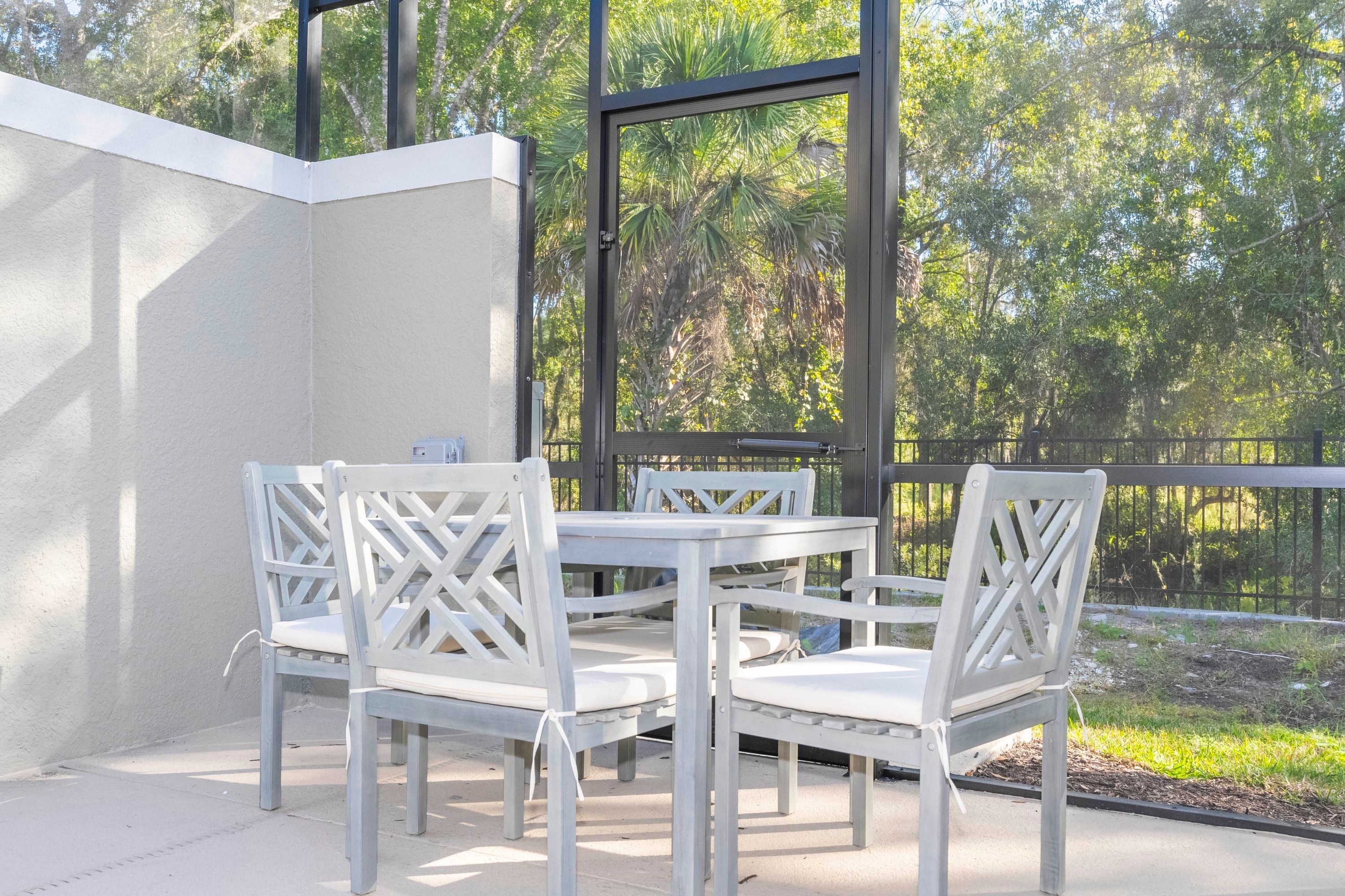 Een terras met een tafel en vier stoelen, een glazen deur en uitzicht op bomen.