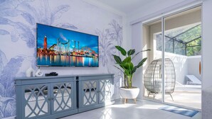 A modern living room with a large flat-screen TV mounted on the wall, a grey console table, a potted plant, and a glass door leading to an outdoor area. - Unwind to Nature s Melody in Storey Lake (Kissimmee)