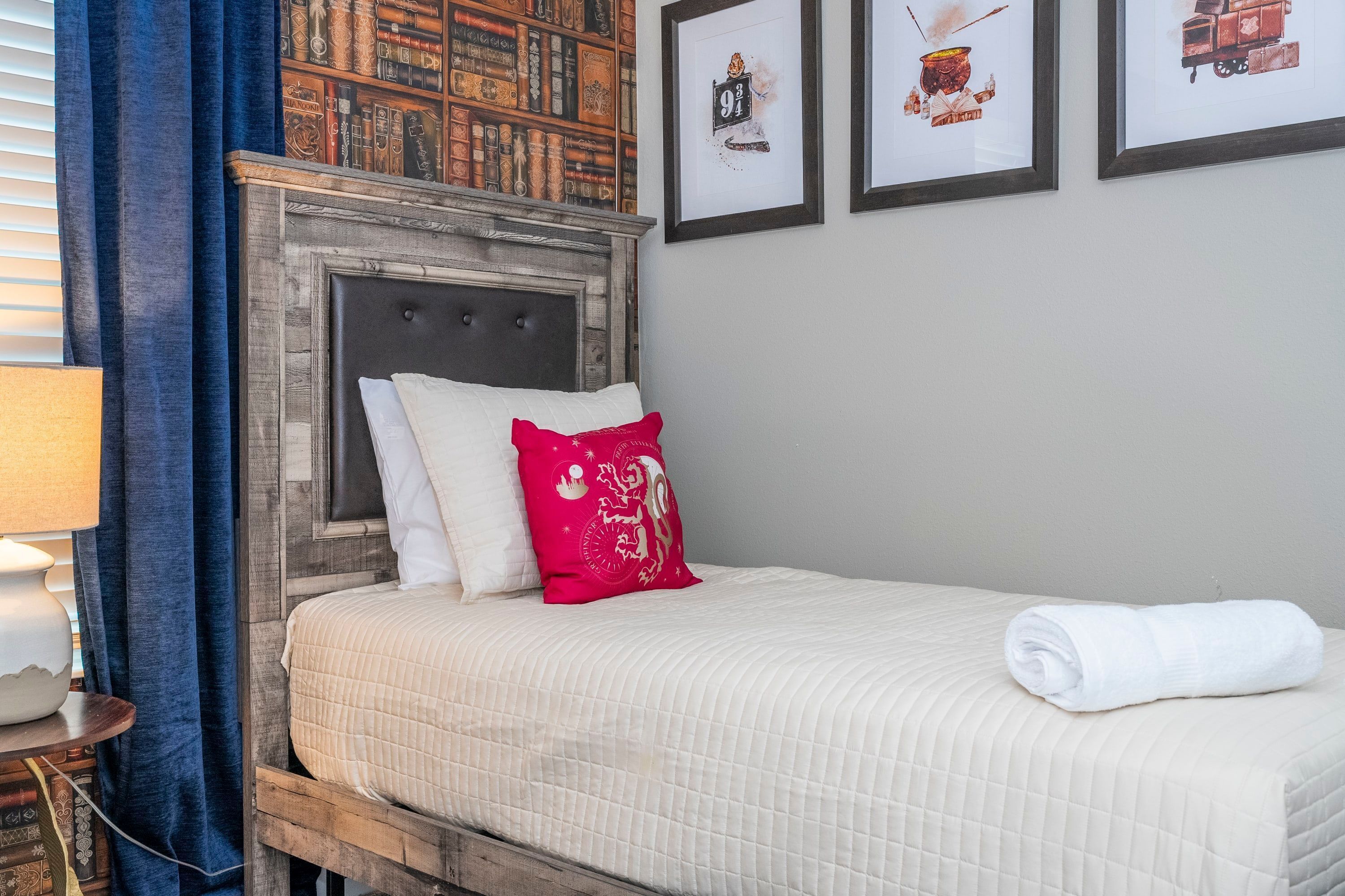 Un lit bien fait, avec une couette blanche matelassée, un coussin décoratif rouge et une serviette blanche roulée posée sur le côté.