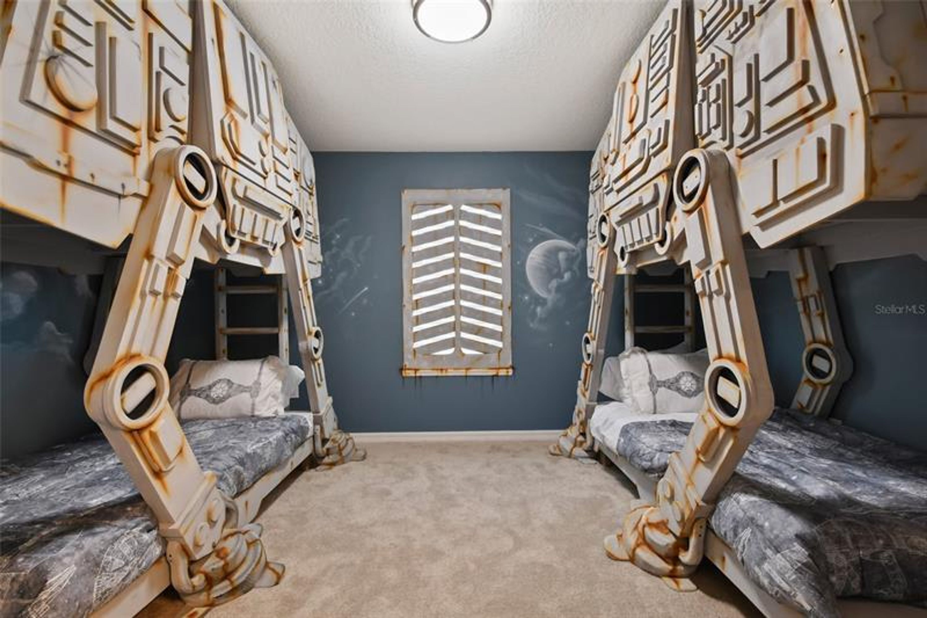 Une chambre avec des lits superposés, une fenêtre au design original et un luminaire au plafond.