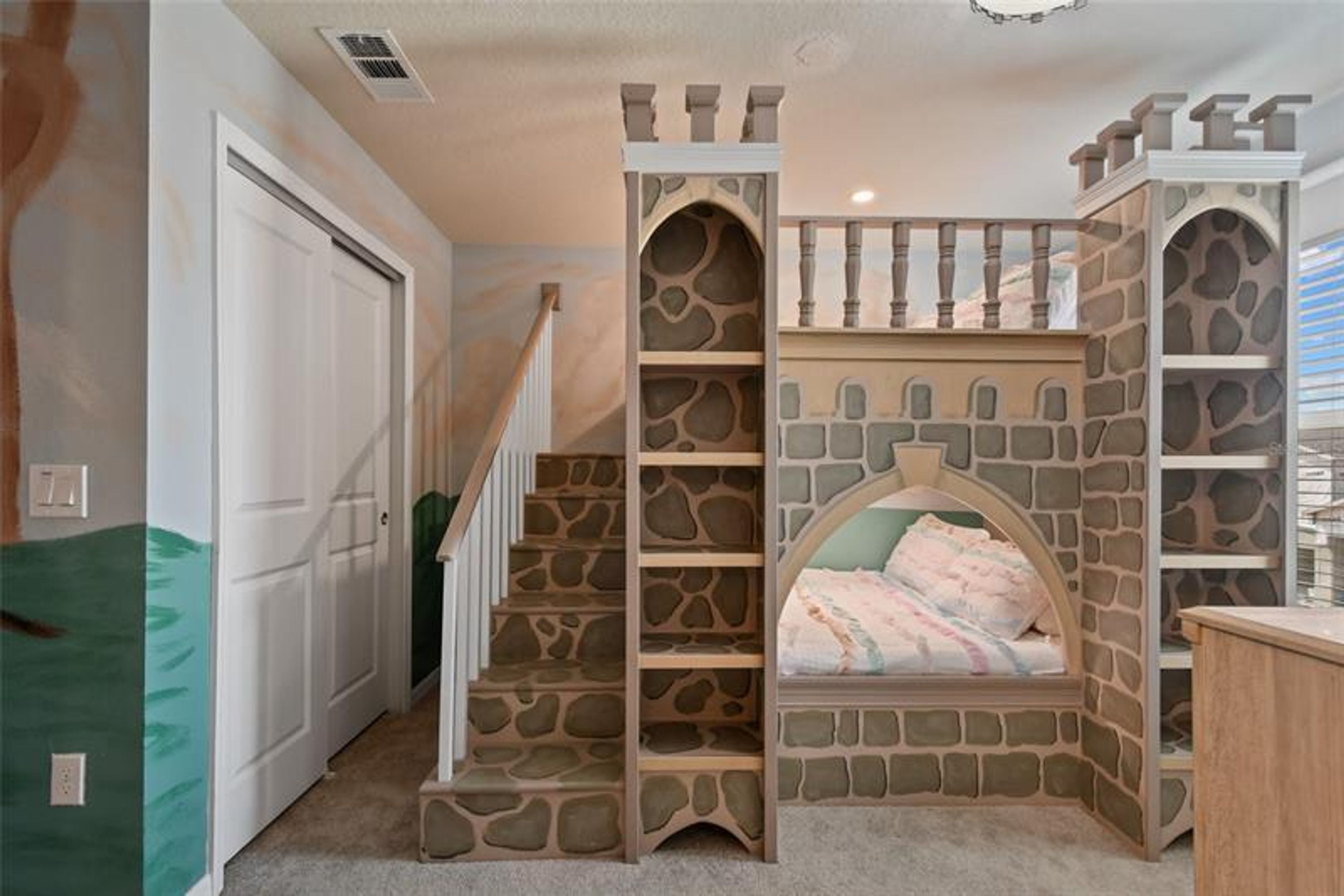 A bedroom with a stone castle-themed bed, a staircase, and a door.