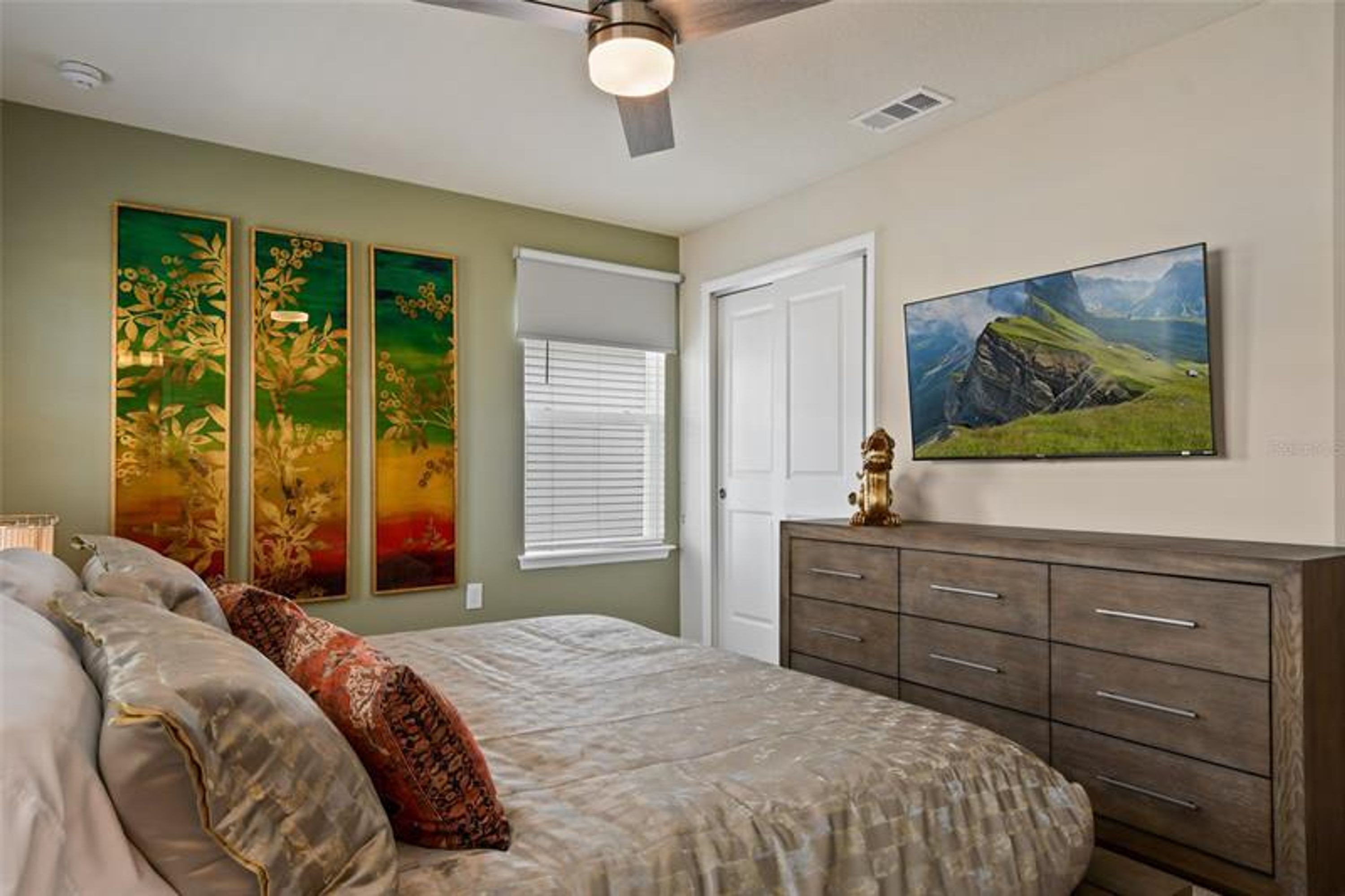 A bedroom with a bed, a dresser, and three paintings on the wall.