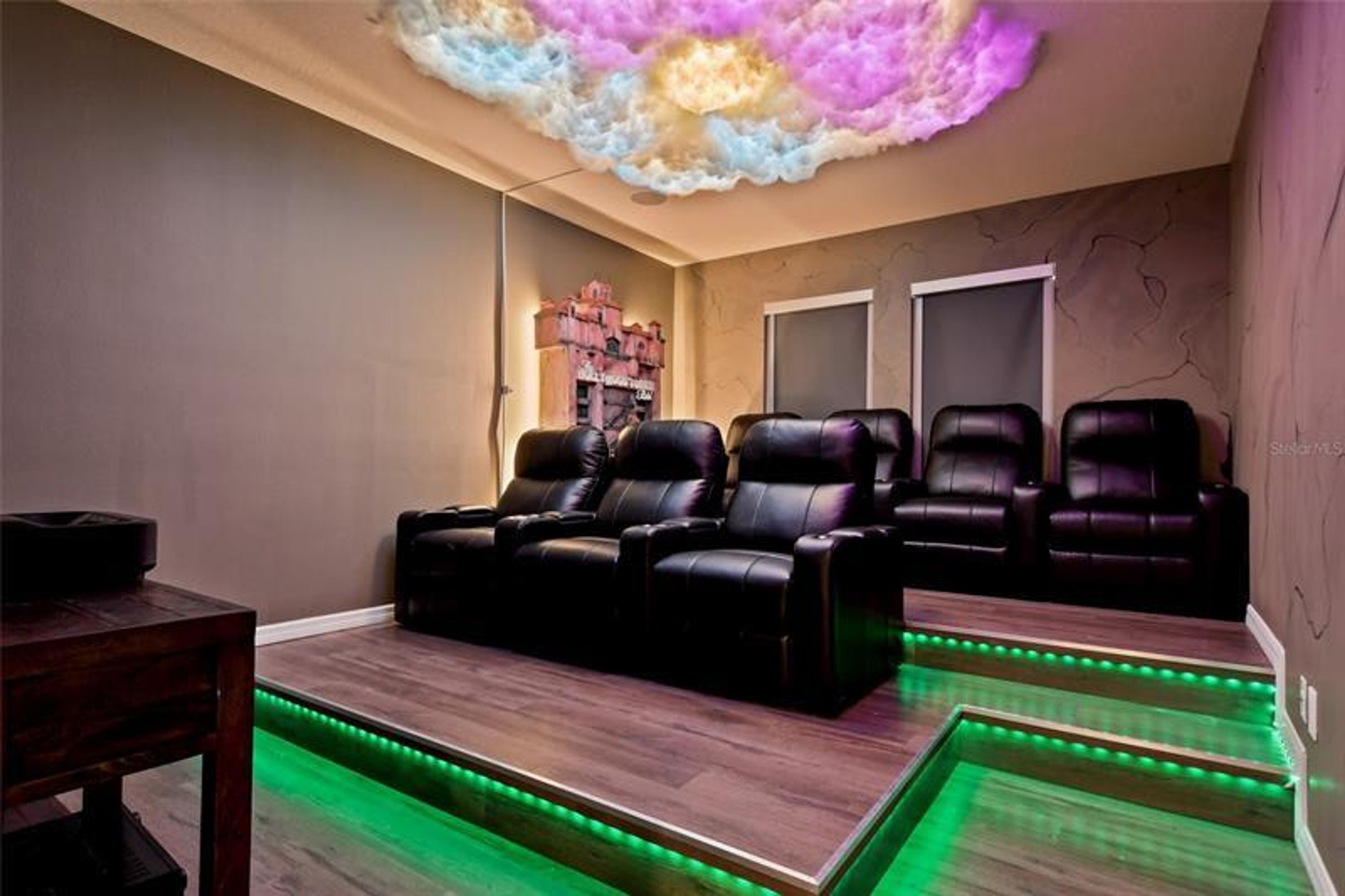 A room with a massage chair area, a wooden table, and a ceiling with a cloud-like light feature.