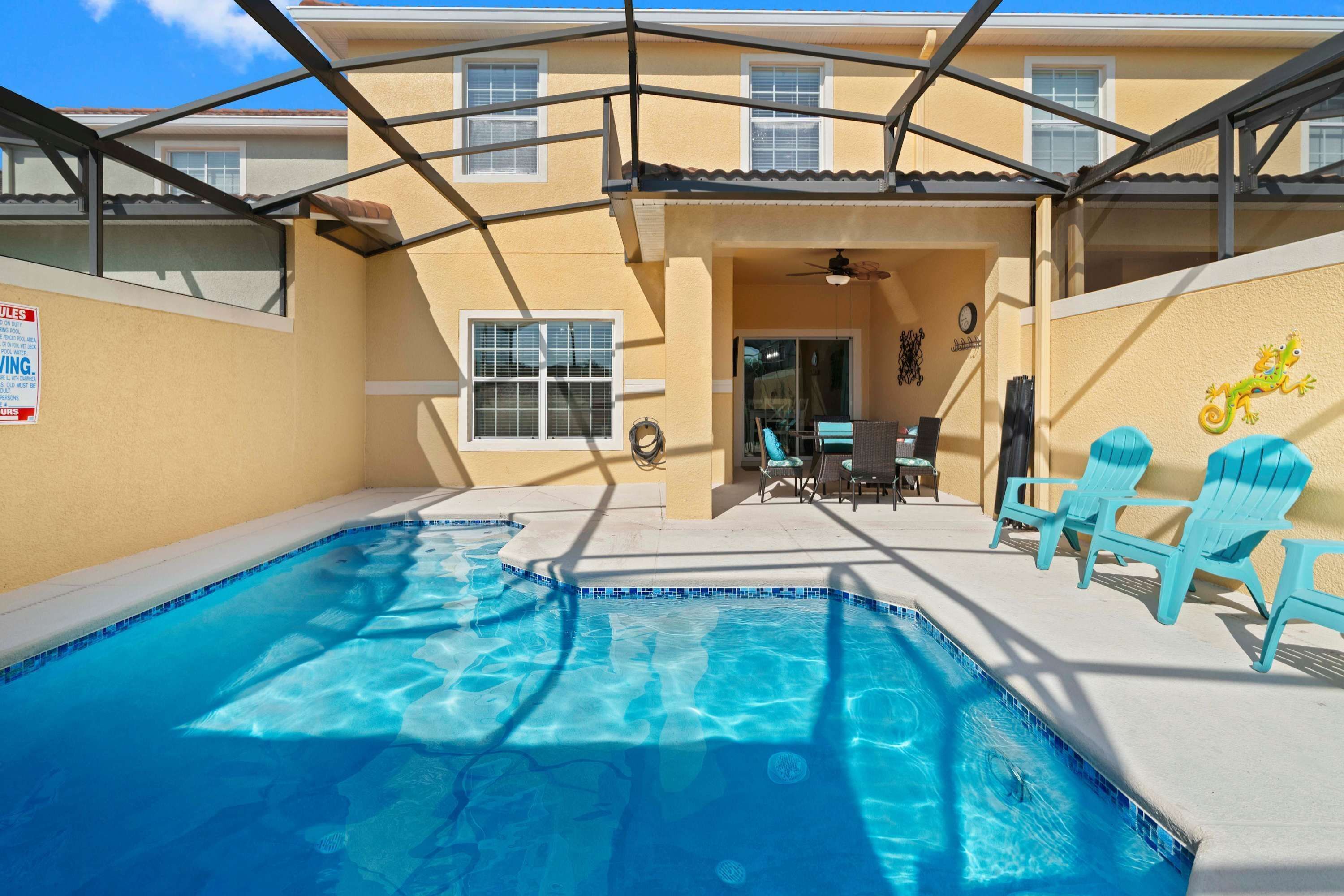 Ein Swimmingpool mit blauen Fliesen, umgeben von einer überdachten Terrasse mit Stühlen und einem Deckenventilator.