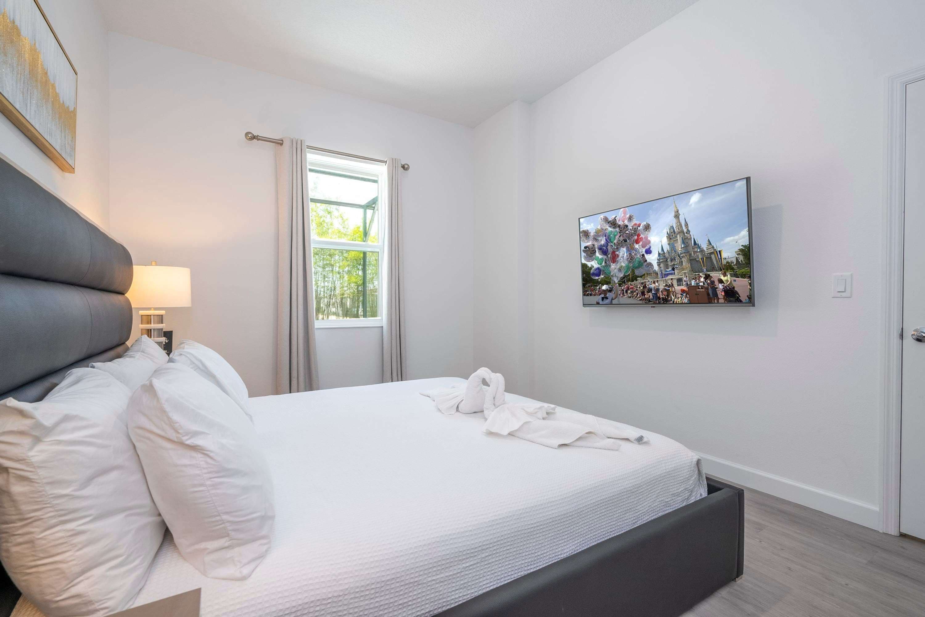 A hotel room with a bed, a TV, a window, and a painting.