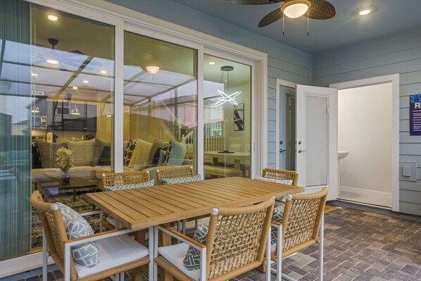 A dining area with a wooden table and wicker chairs, a glass partition, and a ceiling fan. - Brand New 5 bed Villa in Windsor Cay (Clermont)