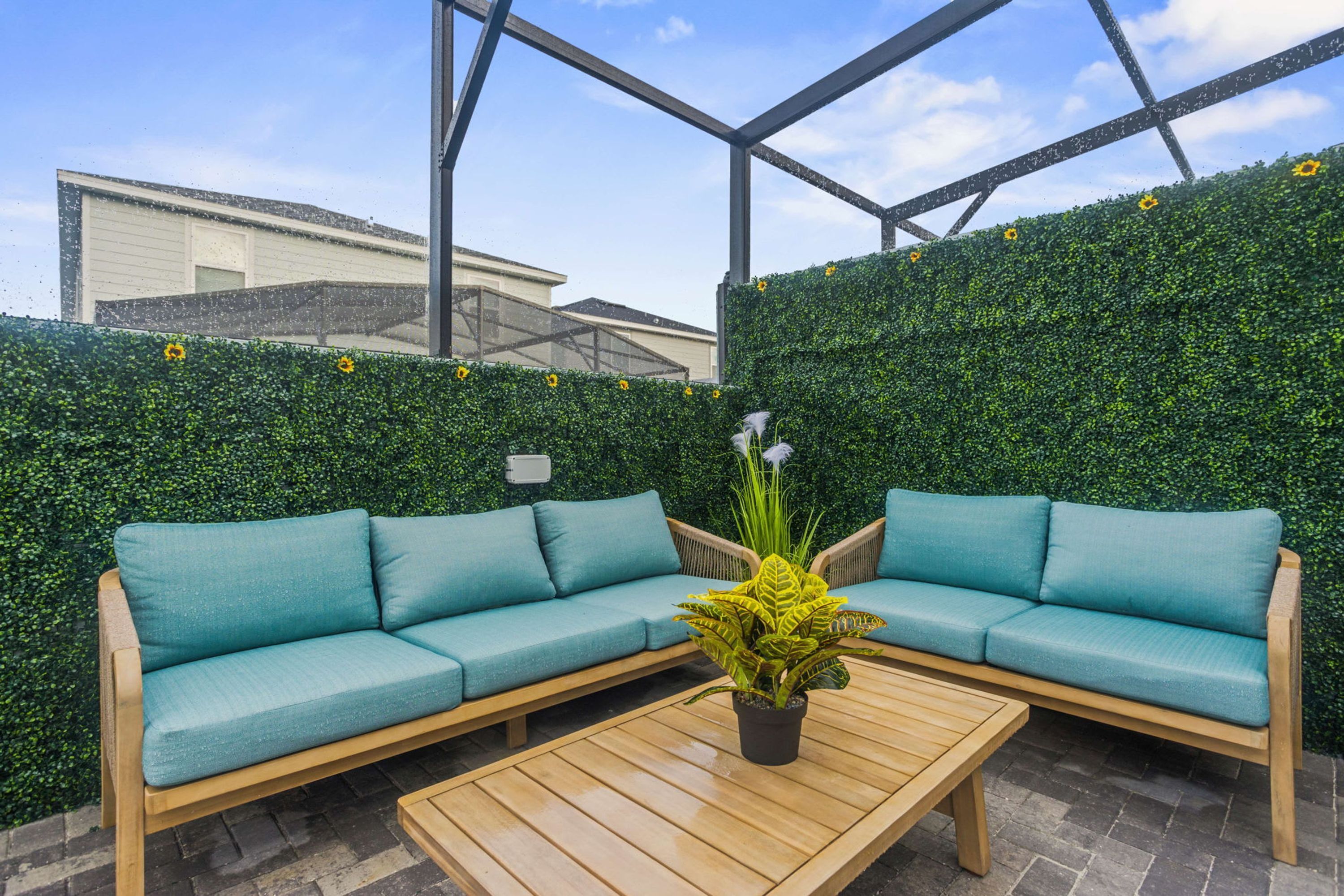 A modern outdoor seating area with a green hedge wall, a wooden bench, and a light-colored sofa.
