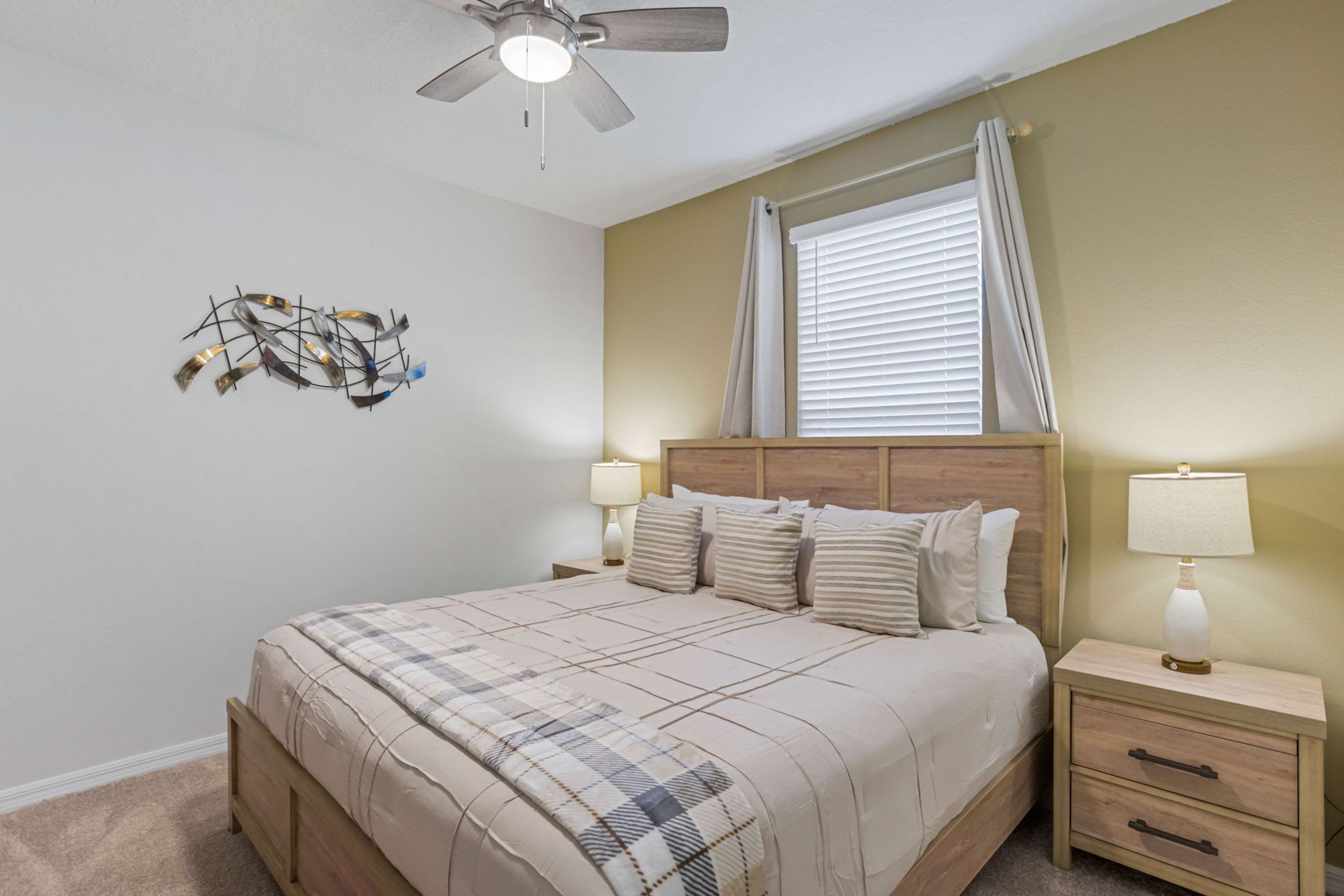 Un dormitorio con cama, mesitas de noche, ventilador de techo y ventana con cortinas.