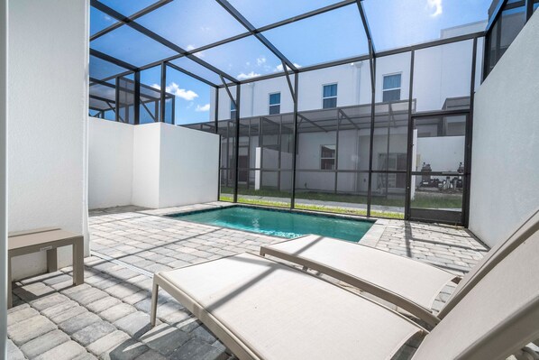 Un área de piscina exterior moderna con paredes de vidrio transparente, piscina y sillones de descanso.