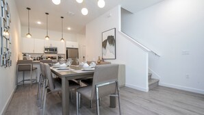 Une cuisine moderne avec des meubles blancs, un four à micro-ondes et un coin repas avec une table dressée pour quatre personnes.
