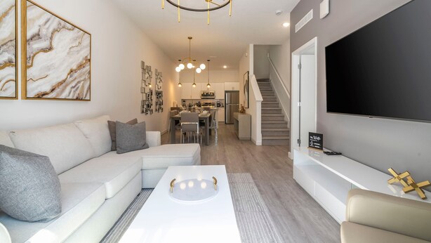 Un salon moderne avec un canapé d’angle, une table basse blanche et un grand téléviseur à écran plat fixé au mur.