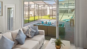 A modern living room with a glass sliding door leading to a patio with a hot tub and outdoor furniture. - Free Pool Heat if you Stay in the Month of November (Davenport)