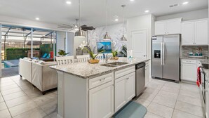 A modern kitchen with white cabinets, a stainless steel refrigerator, and a built-in island with a sink. - Free Pool Heat if you Stay in the Month of November (Davenport)