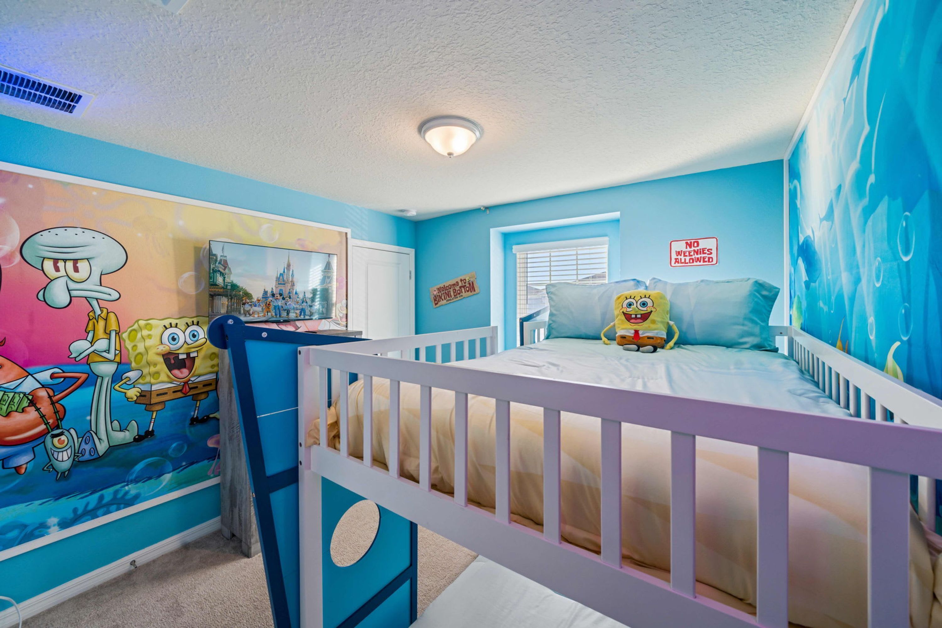Habitación infantil con una cama, un escritorio y un mural en la pared con Bob Esponja.