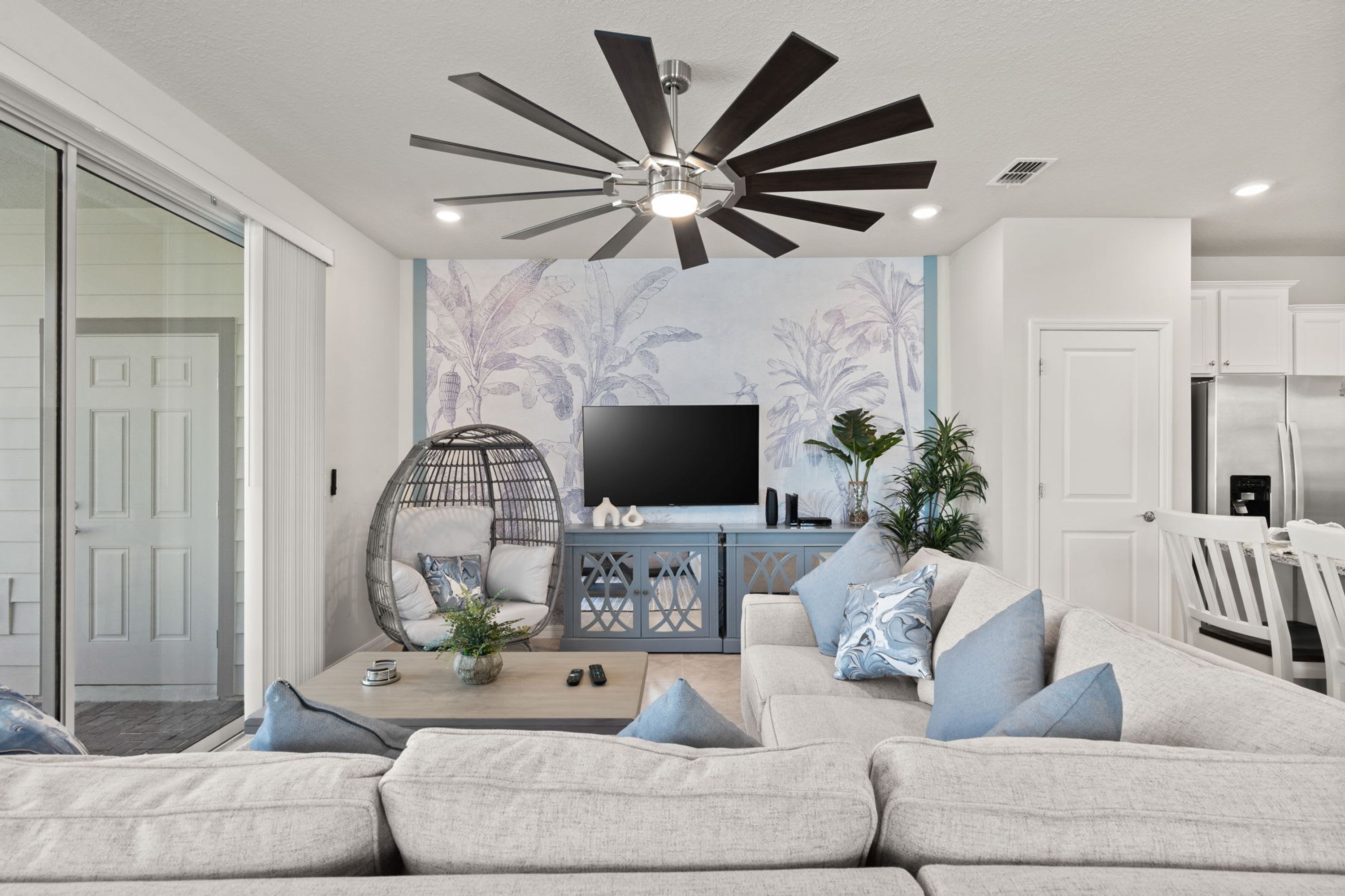 Una sala de estar moderna con un sofá gris, un sillón redondo de mimbre, un televisor de pantalla plana y un ventilador de techo.