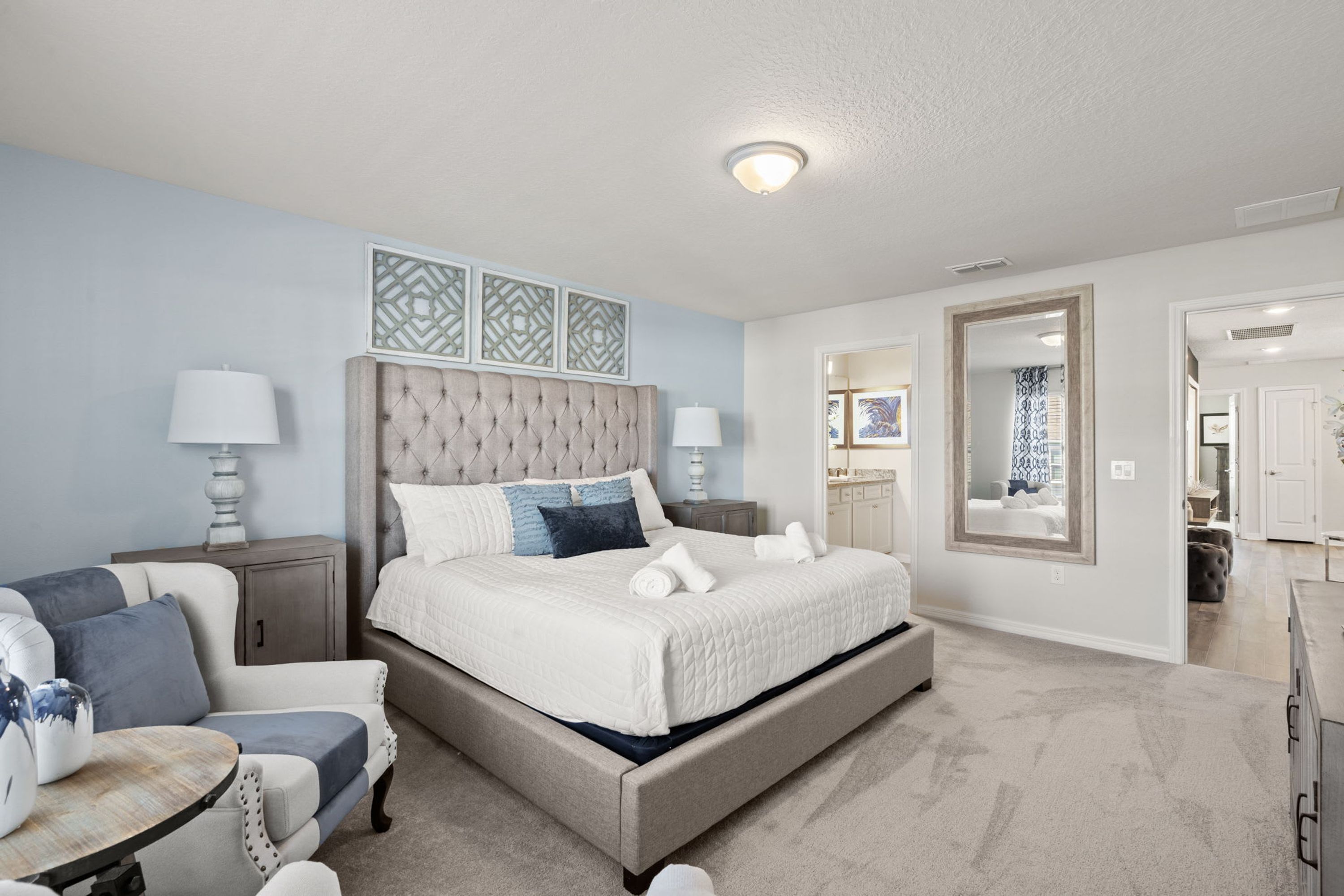 A bedroom with a large bed, bedside tables, a chair, and a mirror.