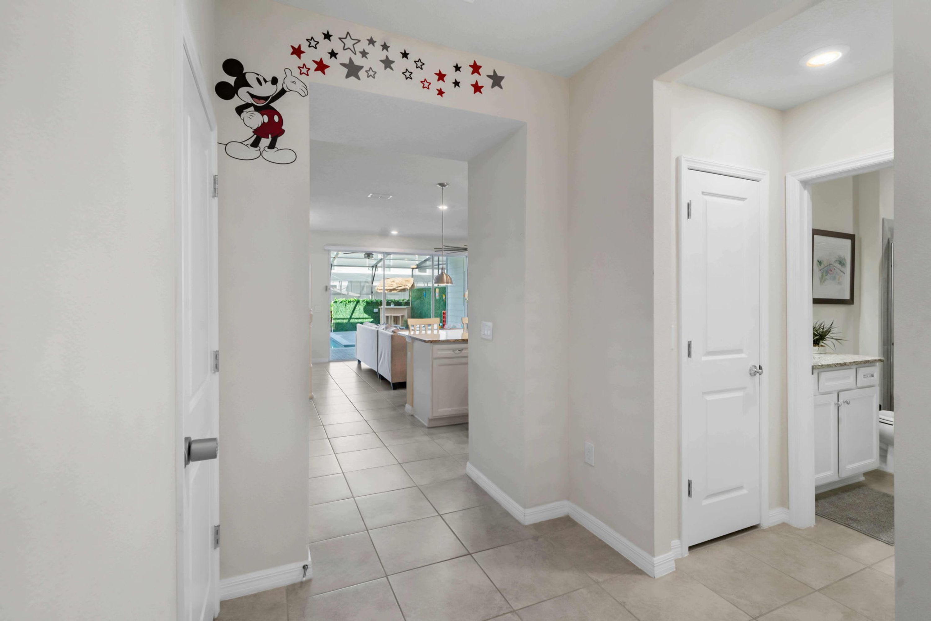 Un pasillo con un adhesivo de Mickey Mouse en la pared, puertas blancas y una cocina al fondo.