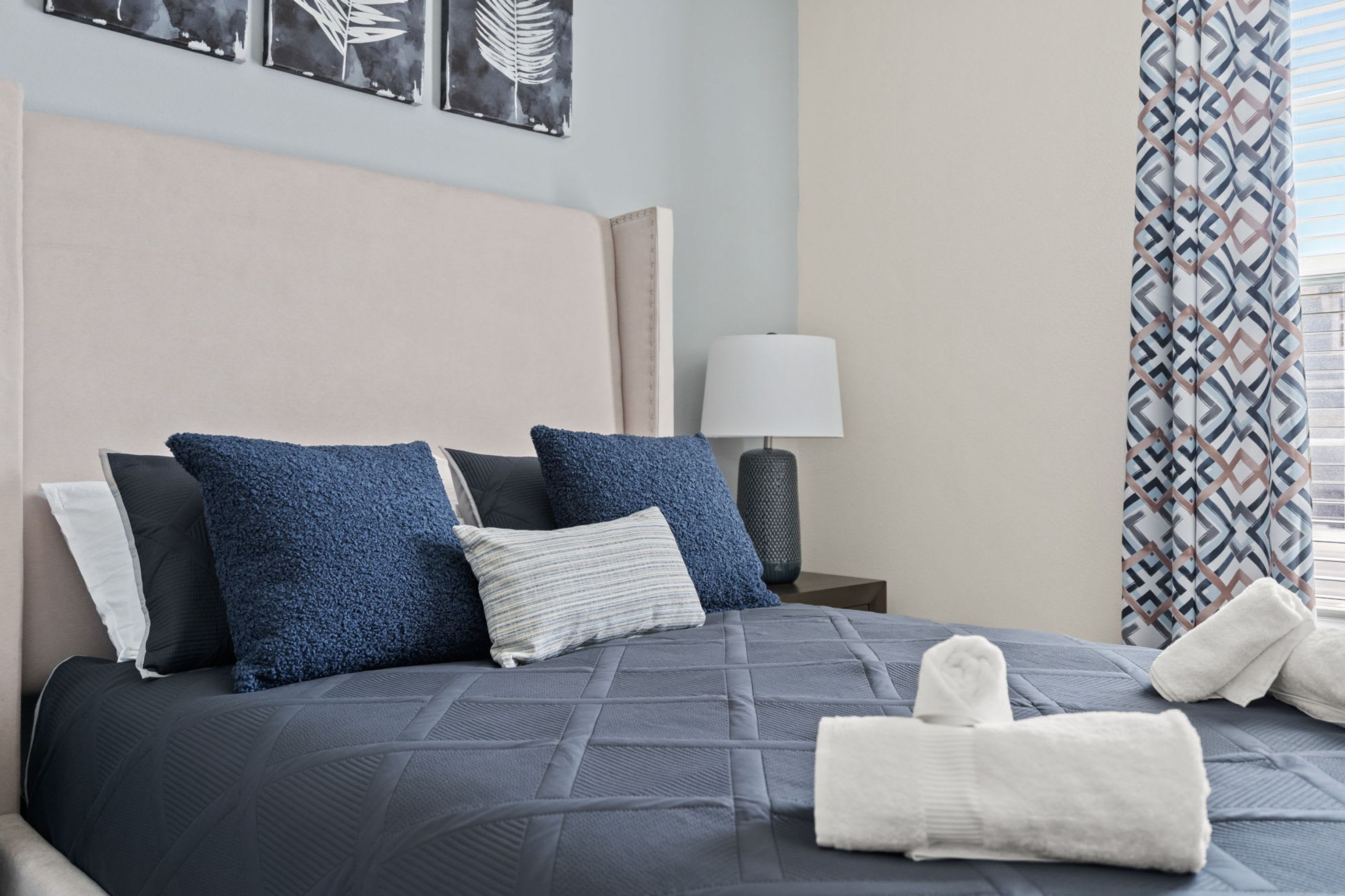Un lit bien fait, recouvert d’une couette bleu foncé, avec plusieurs oreillers et des serviettes soigneusement pliées.