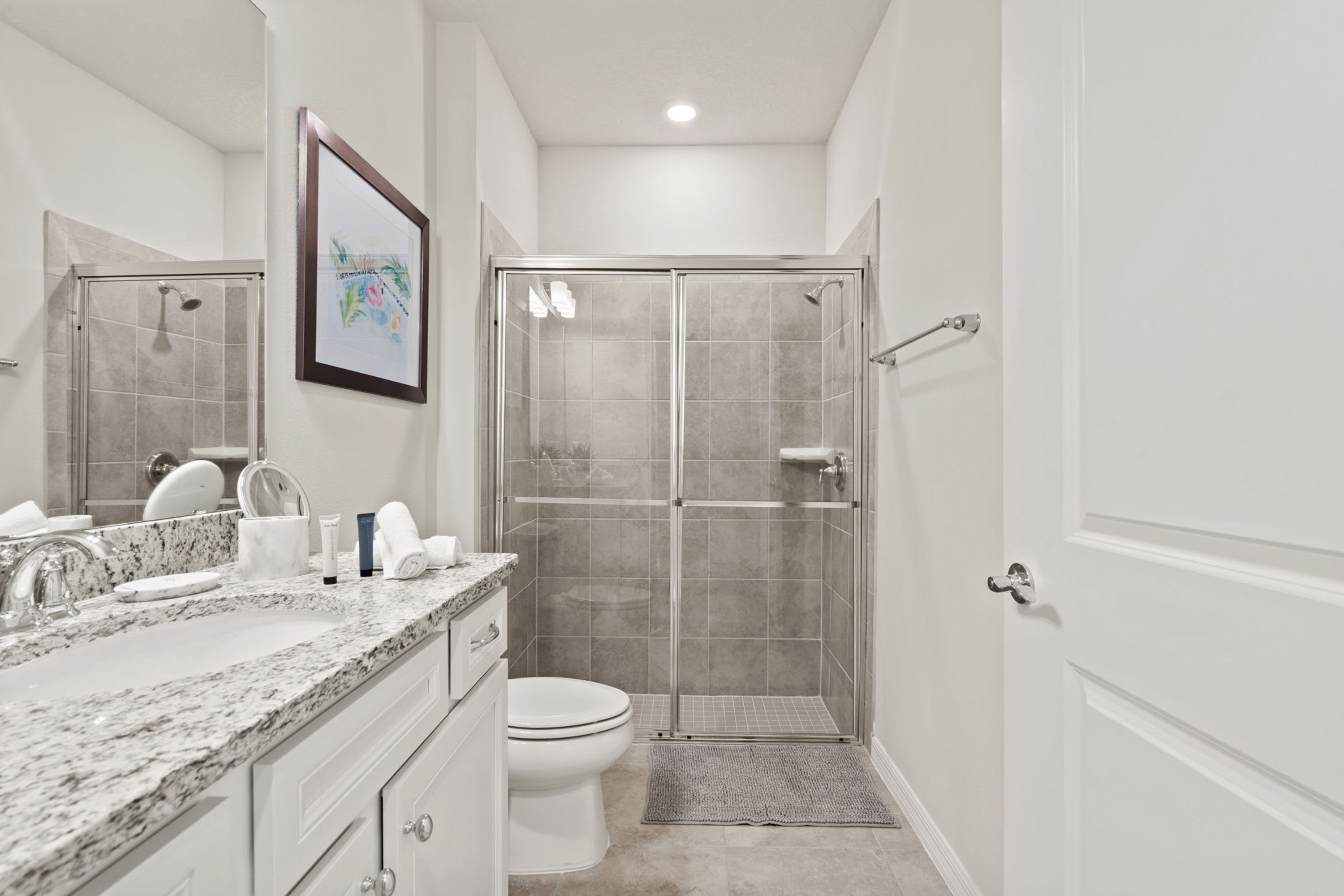 A modern bathroom with a marble countertop, a toilet, a glass shower enclosure, and a framed picture on the wall.