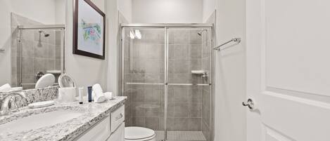A modern bathroom with a marble countertop, a toilet, a glass shower enclosure, and a framed picture on the wall.