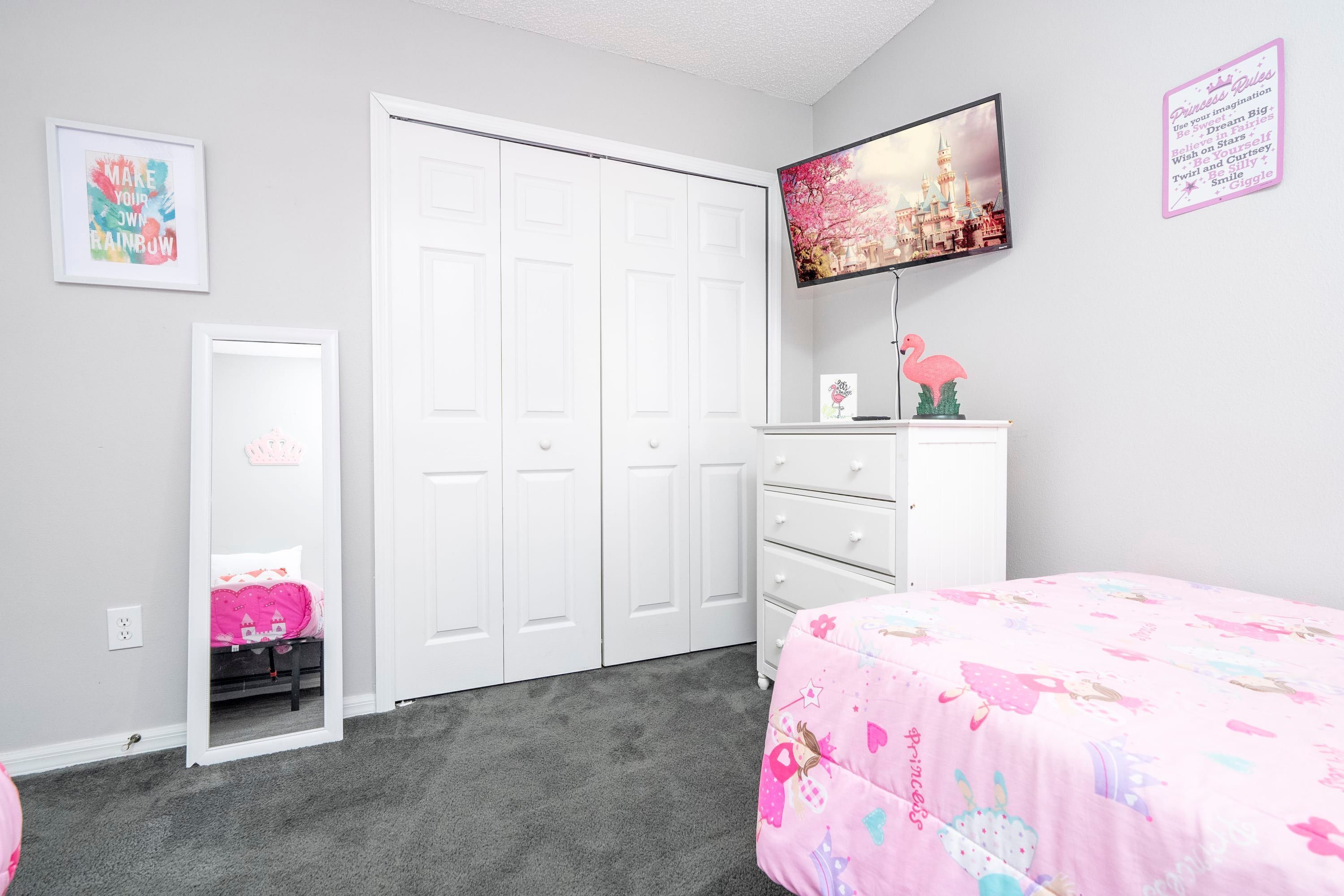 A bedroom with a bed, a dresser, a closet, and a TV on the wall.