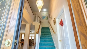 A staircase with blue carpet leading to a second floor, a chandelier, and a door with a red bow. - Enjoy Your own Water Slide and Free Pool Heat if you Stay in November (Kissimmee)