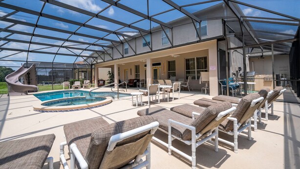 A covered outdoor area with a pool, lounge chairs, and a patio with tables and chairs. - Enjoy Your own Water Slide and Free Pool Heat if you Stay in November (Kissimmee)