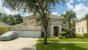 A two-story house with a garage, a covered car, and a well-maintained lawn. - Enjoy Your own Water Slide and Free Pool Heat if you Stay in November (Kissimmee)